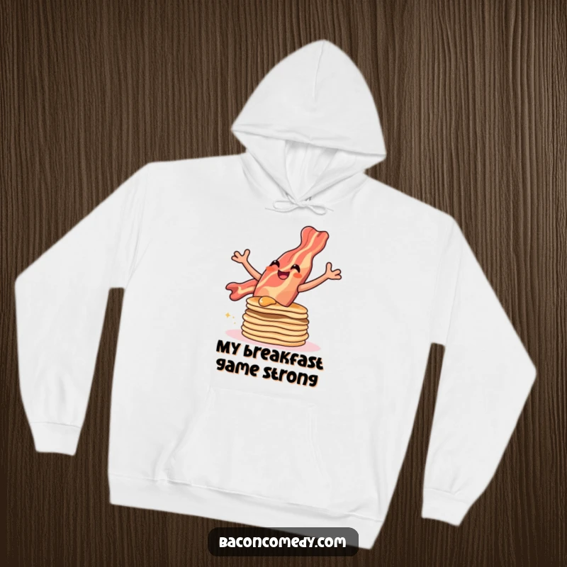 Funny hoodie with a smiling bacon strip soaring over a stack of pancakes, capturing a moment of pure joy.